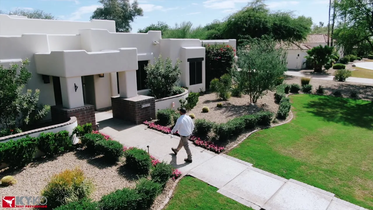 Drone shot of a KY-KO technician walking up to a white stucco home