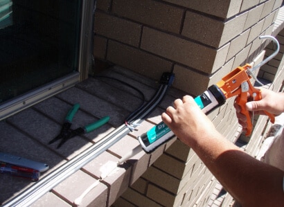 A KY-KO Pest technician puts a line of caulk on the exterior of this building to adhere this pigeon deterrence system to the window sill.