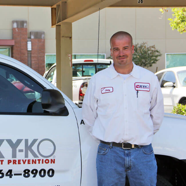 A trusted KY-KO Pest technician stands in front of a KY-KO service vehicle before heading out to their next inspection.