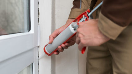 A KY-KO pest technician uses a caulking gun to apply caulk around this home's door frame, sealing pests out of the home.